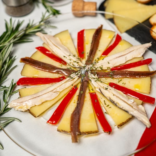 Spanish tapas dish with cheese slices, red peppers, and anchovies arranged in a circle.