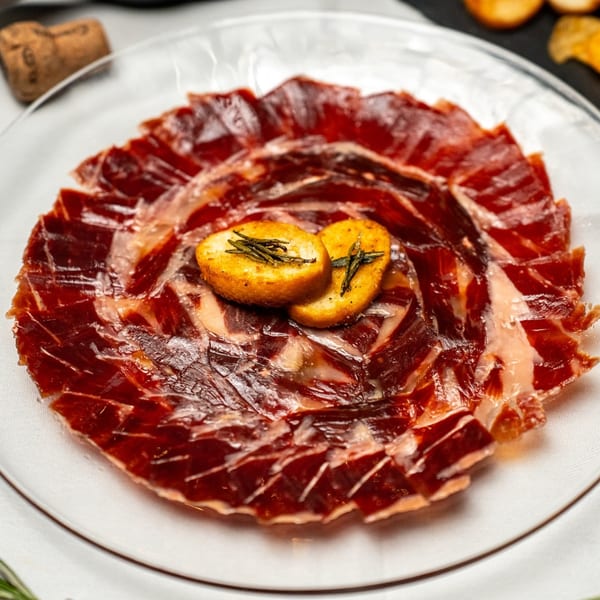 Thinly sliced Spanish Jamón Serrano arranged in a circle with two toasted bread pieces on top.