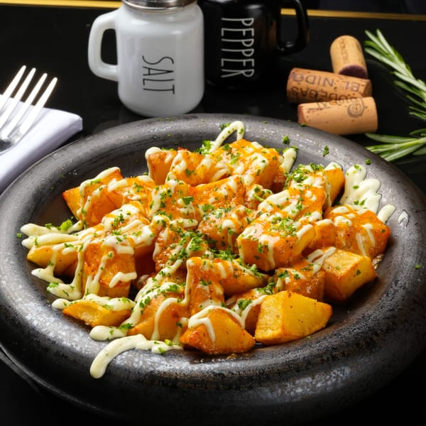 Patatas bravas, fried potato cubes with spicy sauce and aioli, garnished with parsley in a dark bowl.