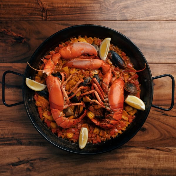 Xixon's Spanish paella with whole lobsters, mussels, clams, and lemon wedges in a black pan.