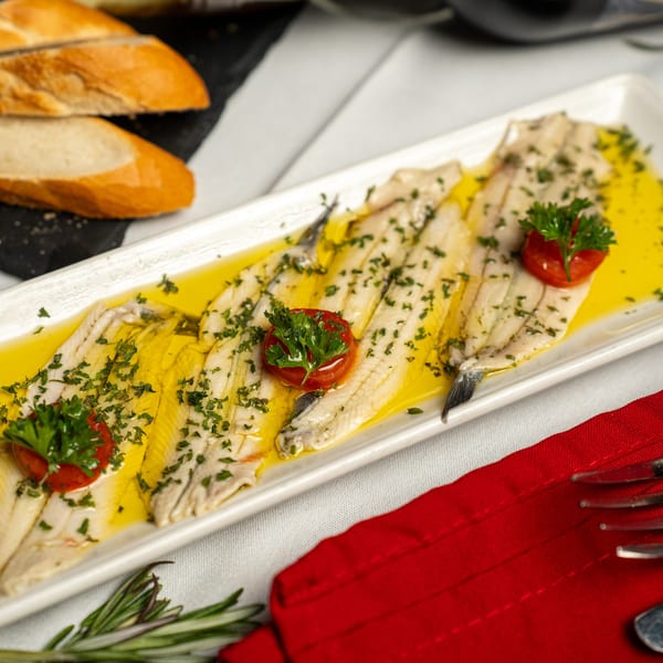 Spanish boquerones en vinagre, marinated anchovies with olive oil, parsley, and cherry tomatoes, served with bread.