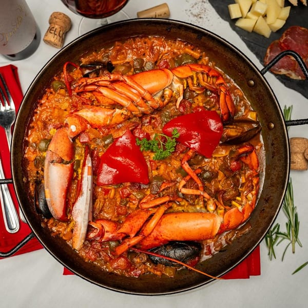 A large paella pan filled with Xixon's lobster paella, garnished with red peppers and parsley.