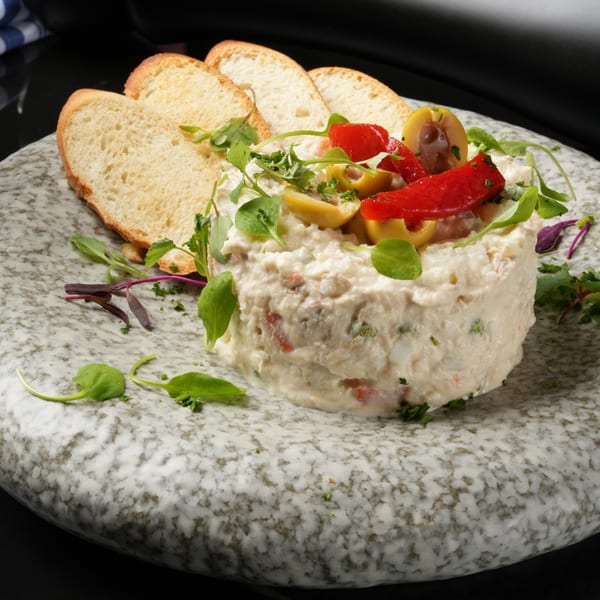 Ensaladilla Rusa, a Spanish potato salad, garnished with red peppers, olives, and microgreens, served with bread.